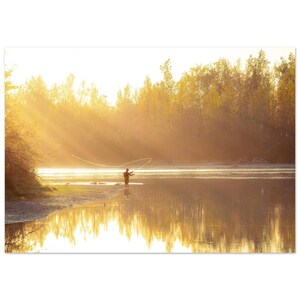 May include: A scenic photograph of a person fly fishing in a river at sunrise. The sun's rays pierce through the trees, creating a golden glow. The water reflects the trees and the sky, adding to the serene atmosphere.