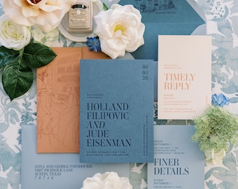 May include: Wedding invitation suite with blue and peach stationery, featuring floral accents and a ring box. The invitations include the names Holland Filipovic and Jude Eisenman, with event details. The suite is arranged on a floral patterned background.