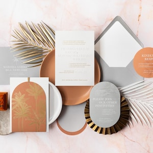 May include: An assortment of wedding stationery, including invitations, RSVP cards, and envelopes, arranged on a marble surface. The invitations feature elegant typography and a warm color palette with gold accents. A ring box is also present.