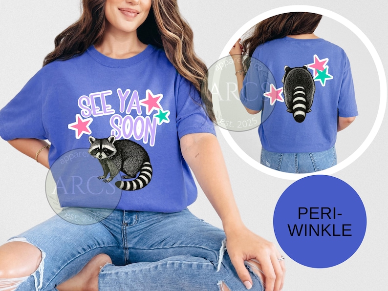 May include: Periwinkle blue t-shirt with a raccoon graphic and the text "See Ya Soon". The design includes pink and green stars. The back of the shirt also features a raccoon and stars.