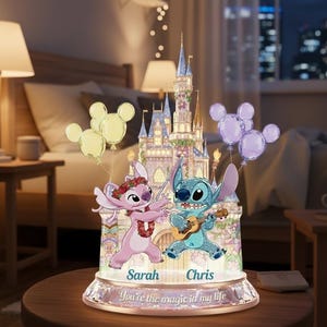 May include: A decorative night light featuring a castle and cartoon characters. The light has a base with the text "You're the magic in my life" and names "Sarah" and "Chris". The characters are holding balloons.