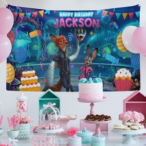 Op de afbeelding: Een verjaardagsfeestje met een achtergrond met personages uit Zootopia en de tekst "Happy Birthday Jackson". De sc&egrave;ne omvat een taart, cupcakes en diverse roze en blauwe decoraties, met ballonnen op de achtergrond.