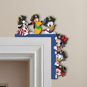 Peut inclure: Un coin décoratif avec des personnages Disney déguisés en pirates. Dingo, Pluto et Donald Duck sont en haut, tandis que Minnie, Daisy et Mickey apparaissent sur le côté. Les personnages portent des chapeaux et des tenues de pirates.