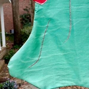 May include: Close-up of a Christmas stocking with a red top and a mint green body. Silver glitter lines the edges and curves down the stocking. The stocking is made of a shiny fabric.