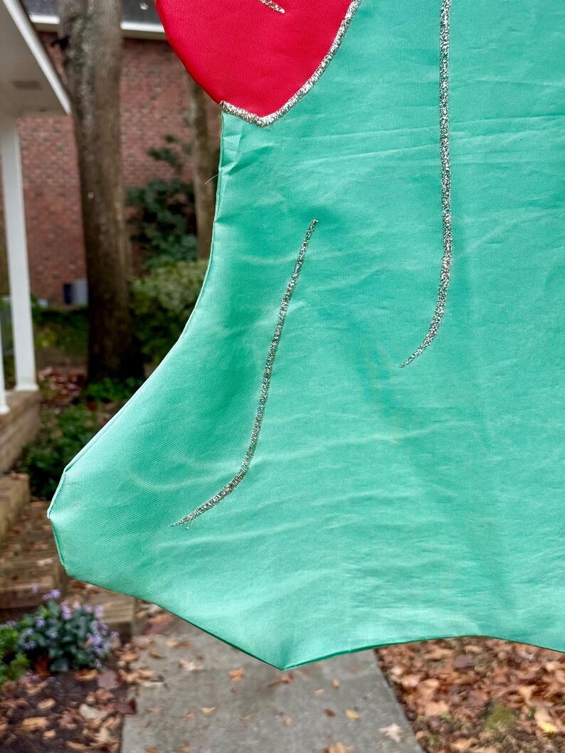 May include: Close-up of a Christmas stocking with a red top and a mint green body. Silver glitter lines the edges and curves down the stocking. The stocking is made of a shiny fabric.