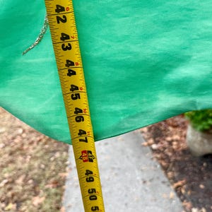 May include: A bright green fabric is measured with a yellow tape measure. The tape measure shows measurements from 41 to 53 inches. A small, gold-colored embellishment is visible on the fabric.