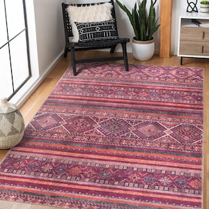 May include: A patterned rectangular rug in shades of red, orange, and purple. The rug features geometric diamond and striped designs. The rug is placed on a wooden floor. The rug's design creates a vibrant and textured look.