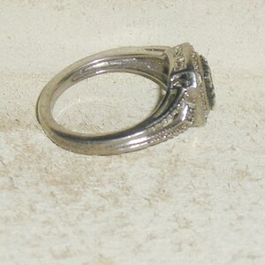 May include: A silver ring with a black stone surrounded by smaller clear stones.