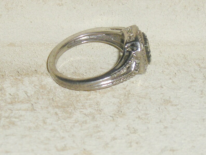 May include: A silver ring with a black stone surrounded by smaller clear stones.