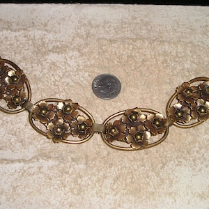 May include: A vintage gold-tone bracelet featuring an oval design with floral clusters. The bracelet is composed of multiple linked oval sections, each adorned with detailed flower embellishments. A dime is included for size reference.