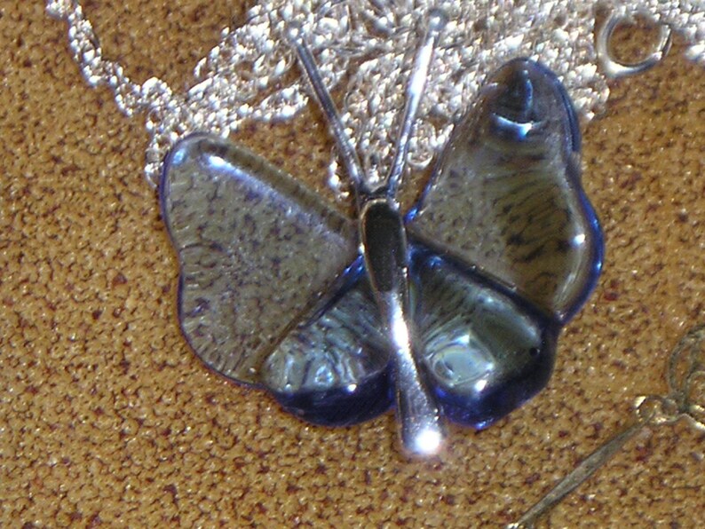 May include: A silver chain necklace with a blue glass butterfly pendant. The butterfly has a detailed design and a silver accent.