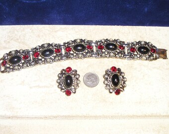 May include: A silver tone bracelet and earrings set with black oval cabochons, red rhinestones, and faux pearls.