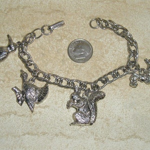 May include: A silver charm bracelet with a variety of animal charms, including a duck, a squirrel, and a bird. The bracelet is made of a silver chain and has a lobster clasp.