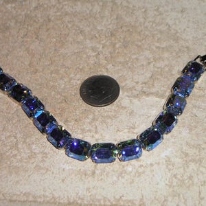 May include: A blue and iridescent crystal bracelet with a silver clasp. The bracelet is made of rectangular-shaped crystals.