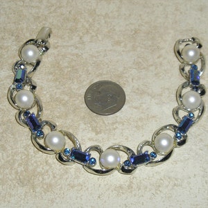 Puede incluir: Una pulsera de plata con perlas falsas y pedrería azul.