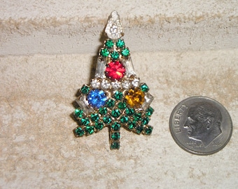 May include: A green rhinestone Christmas tree brooch with red, blue and yellow rhinestones in the centre.