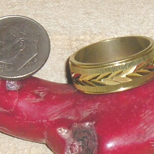 May include: A gold-toned ring with a textured band and a design of gold-colored leaves. The ring is sitting on a red surface.