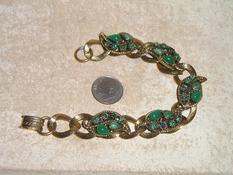 May include: A gold tone bracelet with a chain link design. The bracelet is decorated with green teardrop-shaped stones and smaller green rhinestones.