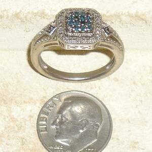 May include: A silver ring with a square-shaped blue diamond surrounded by smaller white diamonds. The ring is next to a US dime for size comparison.