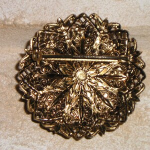 K&ouml;nnte beinhalten: Verzierte goldfarbene Brosche mit detailliertem Blumen- und Filigran-Design. Die R&uuml;ckseite hat einen Nadelverschluss f&uuml;r sicheren Halt. Die Brosche hat eine Vintage-&Auml;sthetik, perfekt, um jedem Outfit einen Hauch von Eleganz zu verleihen.