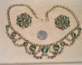 May include: A vintage green and gold rhinestone necklace and earrings set. The necklace features a delicate chain with a repeating pattern of green stones and gold accents. The earrings are a matching pair of green and gold stones.