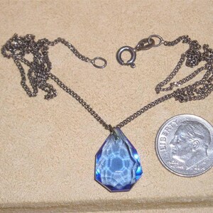 May include: A silver chain necklace with a blue crystal pendant. The pendant is faceted and has a teardrop shape.