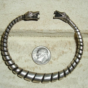 May include: Silver snake bracelet with two snake heads on the ends. The bracelet is coiled and has a silver finish.