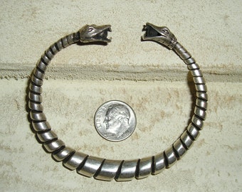 May include: Silver snake bracelet with two snake heads on the ends. The bracelet is coiled and has a silver finish.