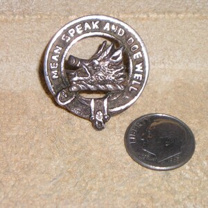 May include: Silver-toned metal pin with a boar's head and the words "Mean Speak and Do Well" around the edge.