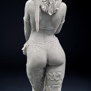 Könnte beinhalten: Graue Figur einer Person, von hinten gesehen, mit einem detaillierten Bikini und Beinbedeckungen. Die Figur hat lange, lockige Haare und ein dekoratives Element, das den Rücken hinunterführt. Das Gesamtdesign ist aufwendig und detailliert.