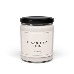 Könnte beinhalten: Eine weiße Sojakerze in einem Glas mit schwarzem Deckel. Auf dem Etikett steht "AI CAN'T DO THIS" in schwarzer Schrift. Darunter steht "SOY CANDLE" und "PINKMILKPRESS".