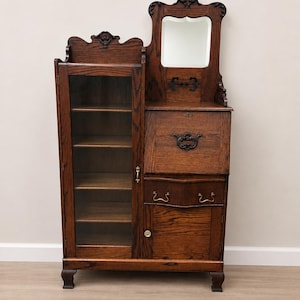 May include: An antique wooden cabinet with a built-in mirror, glass-door display case, and drawers. The cabinet is made of dark-stained wood with ornate carvings and hardware. The mirror is rectangular with a decorative frame. The display case has multiple shelves.