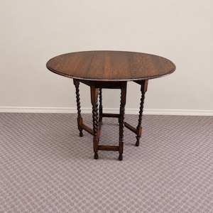 Op de afbeelding: Een ronde, donkere houten klaptafel met een gedetailleerd, gesneden tafelblad en vier gedraaide poten. De tafel heeft een diameter van ongeveer 91 cm wanneer deze volledig is uitgeklapt. De poten hebben een gedraaid touwontwerp.