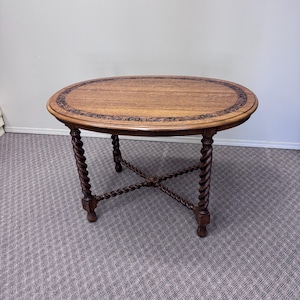 Puede incluir: Mesa ovalada de madera con acabado marrón oscuro. La tapa tiene un borde decorativo y descansa sobre cuatro patas retorcidas y talladas. La mesa mide aproximadamente 76 cm de largo y 51 cm de ancho.