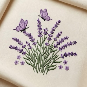 Puede incluir: Diseño bordado de lavanda y mariposas en tonos morados y verdes. Los tallos de lavanda son verdes, con cabezas de flores moradas. Dos mariposas están posadas sobre la lavanda. El fondo es de color crema.