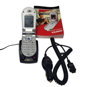 May include: Silver LG VX4500 flip phone with a black charging base, a car charger, and a user manual. The phone is open, displaying a screen. The manual is red and white, with the text "VX4500".