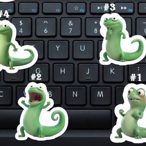 May include: Five green lizard stickers with white borders are displayed on a black keyboard. Each sticker shows a different pose, and they are numbered from 1 to 4. The lizards have expressive eyes and are in various poses.