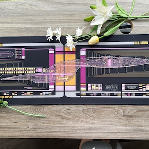 May include: Black rectangular mousepad featuring a schematic of a Galaxy Class starship, with the text "GALAXY CLASS" and "U.S.S. SATURN - NCC-71810". The design includes pink, yellow, and white accents. The mousepad is approximately 30 inches long.