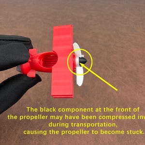 May include: A small red toy airplane with a white propeller and a black component at the front. The text on the image says the propeller may be stuck due to compression during transportation.