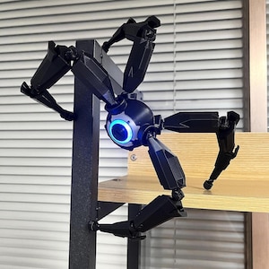 May include: A black, mechanical spider-like robot with multiple articulated legs. The central body features a glowing blue eye-like light. The robot is mounted on a black metal support structure and a wooden shelf.