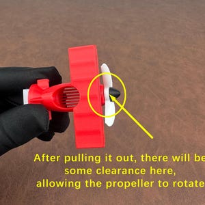 May include: A red toy airplane with white propeller blades. The text on the image reads: "After pulling it out, there will be some clearance here, allowing the propeller to rotate."