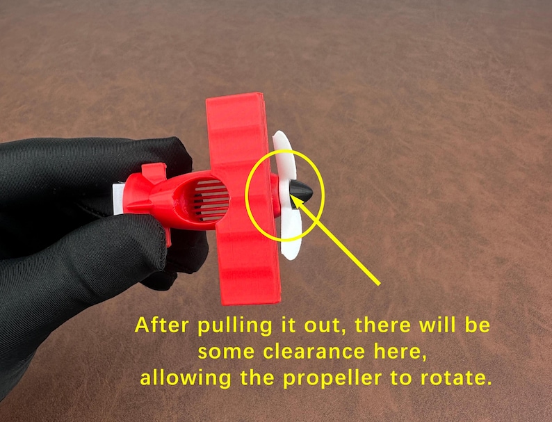 May include: A red toy airplane with white propeller blades. The text on the image reads: "After pulling it out, there will be some clearance here, allowing the propeller to rotate."