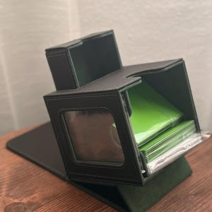 May include: Black and green card holder with a clear window and white stitching. The holder is open, revealing a stack of green cards. The holder is on a wooden surface.