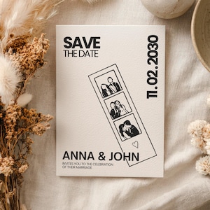 A cream-colored wedding invitation card with the text "SAVE THE DATE" and "ANNA & JOHN". The card features a photo strip with three images of a couple and the date "11.02.2030". The invitation is surrounded by dried flowers and a ceramic bowl.