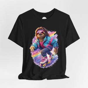 May include: Black t-shirt featuring a cartoon sloth wearing sunglasses, a headband, and a colorful jacket, roller skating on a rainbow background. The sloth has a gold chain and a watch. The design has a retro 80s vibe.
