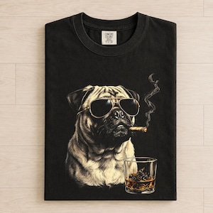 May include: A black crew neck t-shirt featuring a graphic of a pug wearing gold-rimmed aviator sunglasses, smoking a cigar with visible smoke trails, and positioned next to a glass of amber-colored liquid with ice cubes. The label reads Comfort Colors.