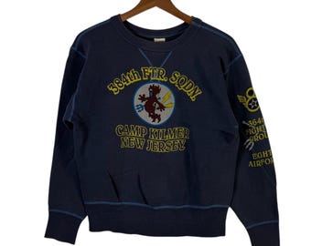 May include: Navy blue sweatshirt with embroidered design. The front features a circular emblem with a devil figure and text: "384th FTR. SQDN. CAMP KILMER NEW JERSEY." The right sleeve has additional text and a winged emblem.