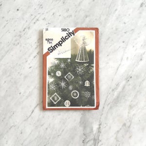 May include: A vintage Simplicity pattern envelope, featuring a Christmas tree with ornaments and an angel. The envelope is labeled "5180" and includes the Simplicity logo. The design includes snowflakes, stars, and bell-shaped ornaments.