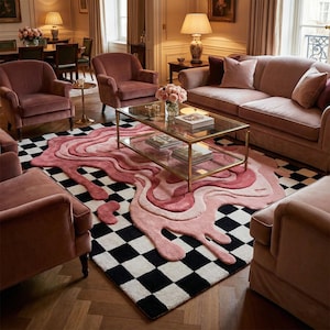 May include: A living room featuring a pink and black checkered rug with a unique, abstract design. The rug is complemented by pink velvet furniture, including a sofa and armchairs. A glass coffee table with a gold frame sits in the center.
