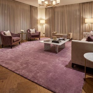 Puede incluir: Un lujoso sal&oacute;n con una gran alfombra suave de color malva. La habitaci&oacute;n incluye dos sillones, un sof&aacute; y una mesa de centro. Las paredes est&aacute;n adornadas con cortinas de tonos neutros, y la habitaci&oacute;n est&aacute; iluminada por una l&aacute;mpara de ara&ntilde;a y l&aacute;mparas de pie.
